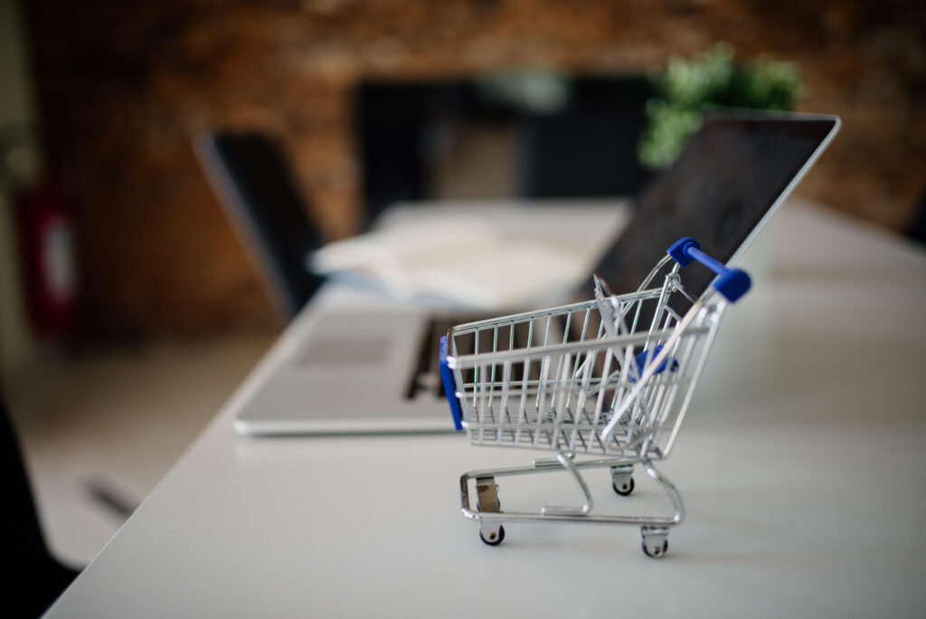 Un petit chariot de courses posé sur une table à côté d'un ordinateur portable, symbolisant le commerce en ligne